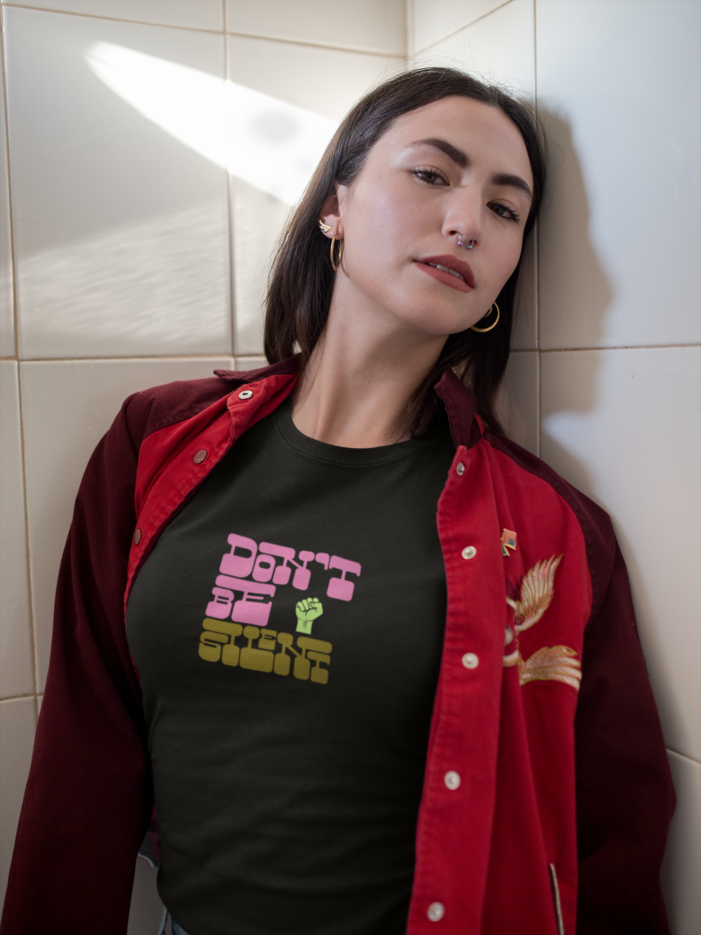 Person wearing a black t-shirt with text and a red jacket against a tiled wall.