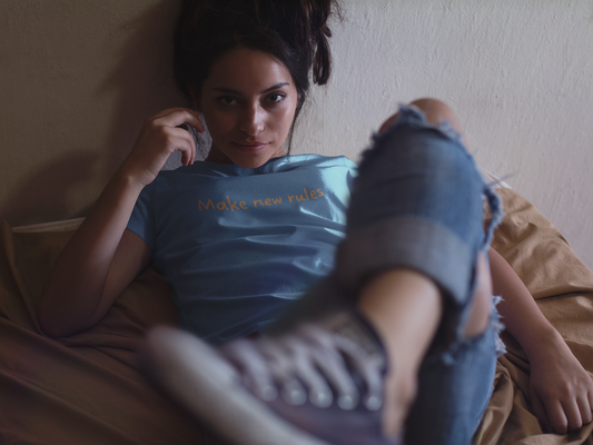 Woman sitting on a bed wearing a blue t-shirt with text and purple sneakers.